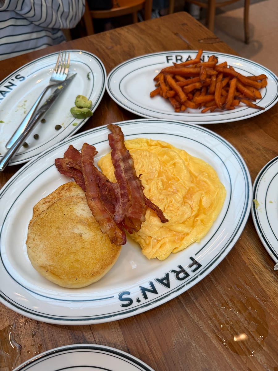 English muffin with scrambled eggs and crispy bacon, sweet potato fries behind