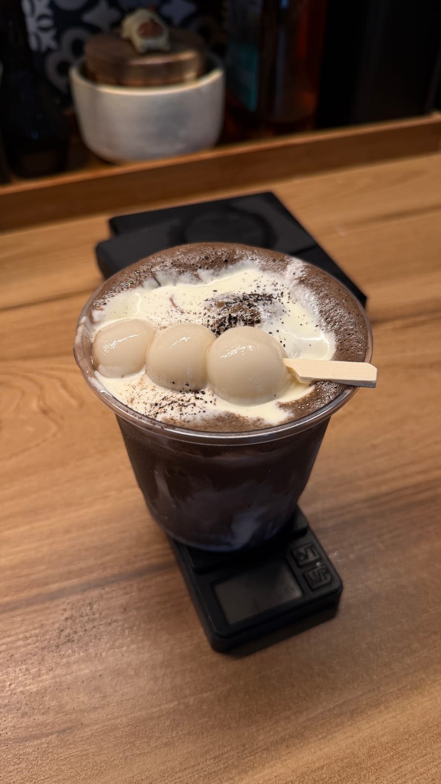 A chocolate drink crowned with mochi dango on a skewer, sitting on a scale