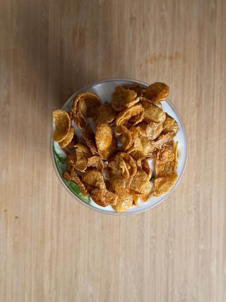A cup piled with cornflake topping, shot from above on a wooden board